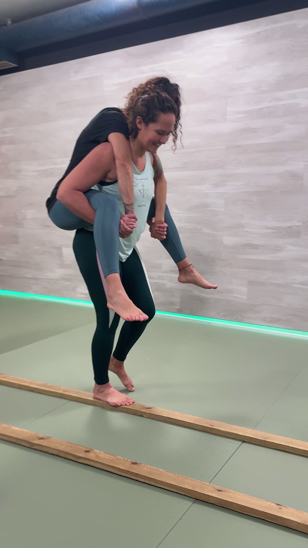 Alumna transportando a una compañera a caballito sobre una viga de madera en el LAB